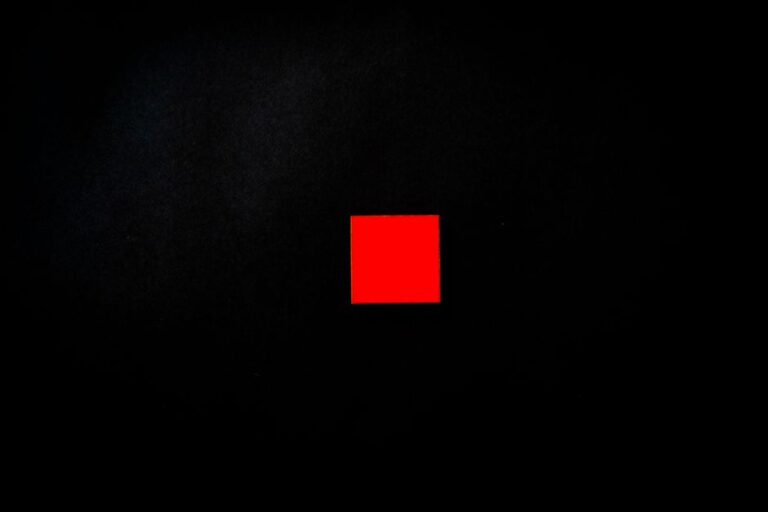 Vivid red square centered on a minimalist black background, creating a striking visual contrast.
